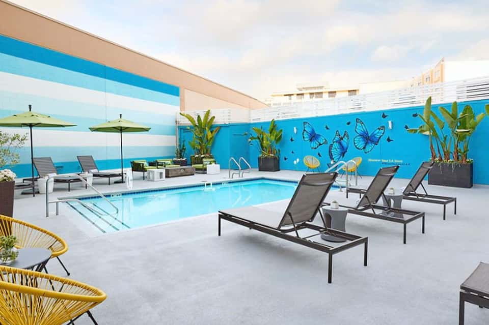 Indoor pool with colorful mural, lounge chairs, umbrellas, and modern architecture