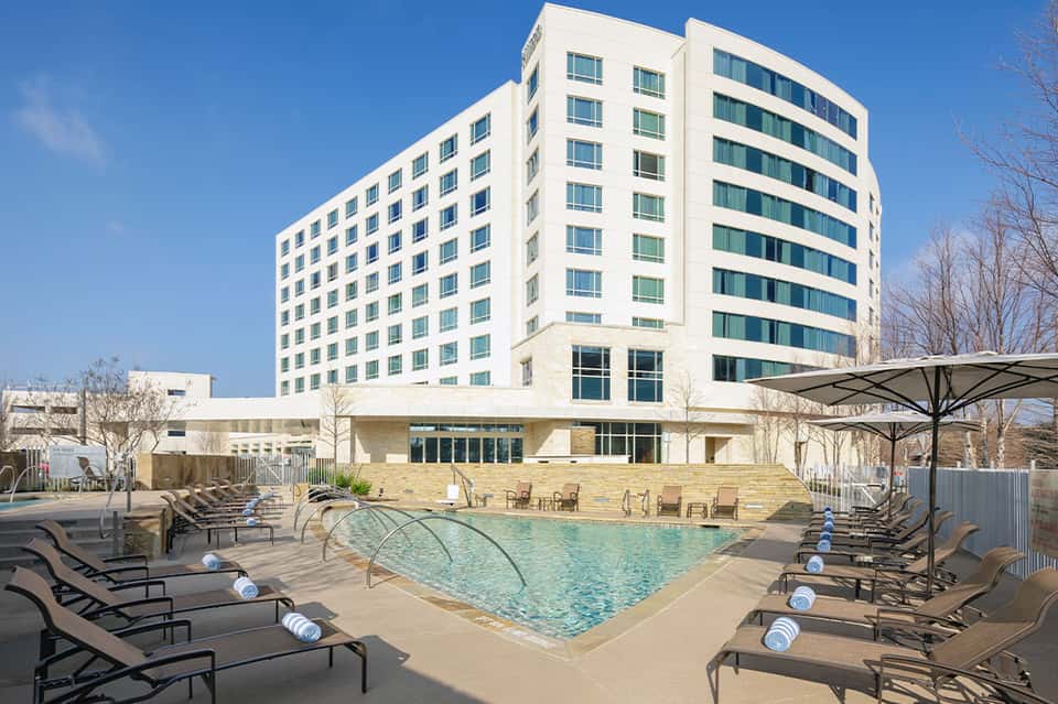 Modern hotel building with ground-level pool, lounge chairs, and umbrellas