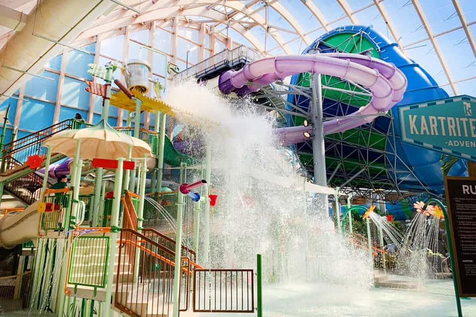 Indoor water park with purple water slide, colorful play structure, and glass ceiling