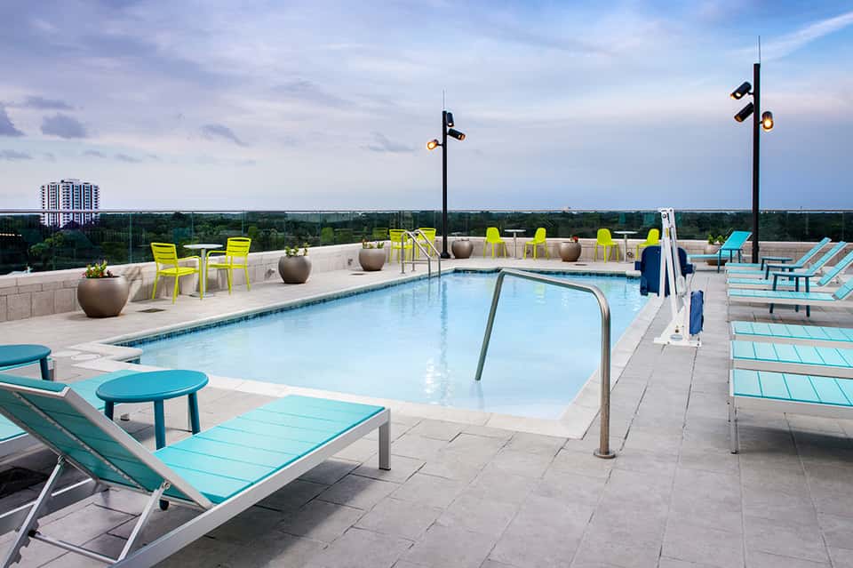 Rooftop pool deck with turquoise loungers, yellow chairs, and panoramic views