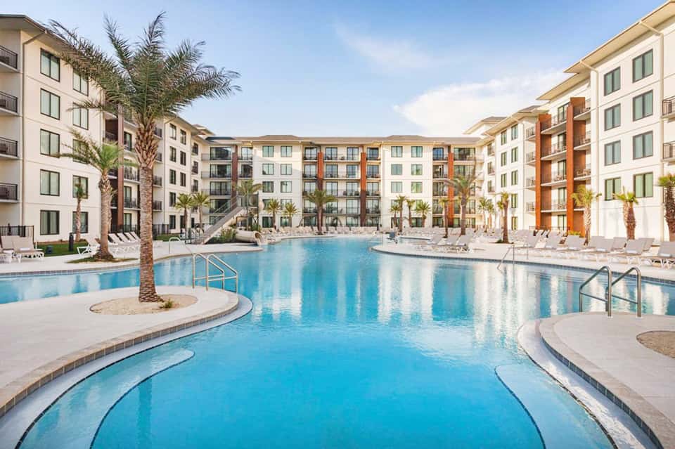 Expansive resort pool courtyard surrounded by multi-story apartment buildings with palm trees and lounge seating