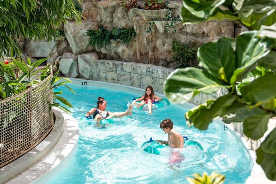 Family enjoying a shallow indoor pool surrounded by stone walls and tropical plants with natural light