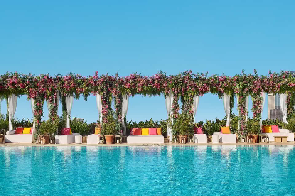 Stunning pool cabana with magenta flower garlands, white curtains, and colorful cushioned seating