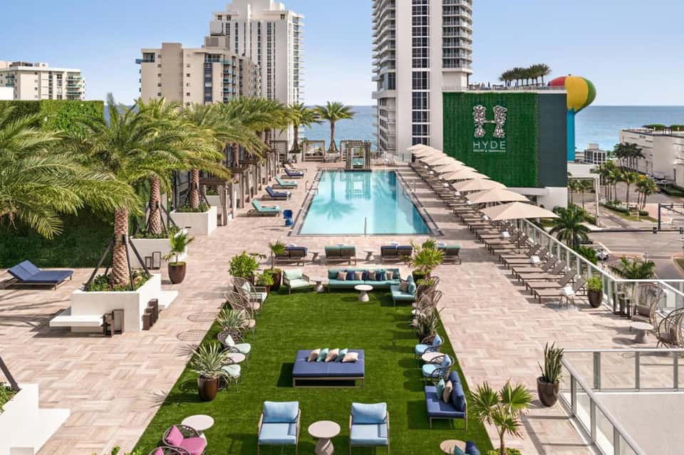 Rooftop pool deck with lap pool, green lawn seating area, ocean view, and palm landscaping