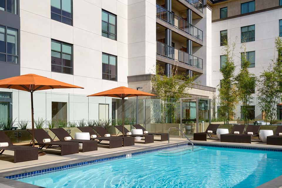 Modern resort pool with orange umbrellas, dark lounge chairs, and contemporary multi-story building