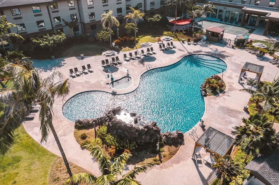 Aerial view of resort pool complex with turquoise water, lounge chairs, and surrounding palm trees