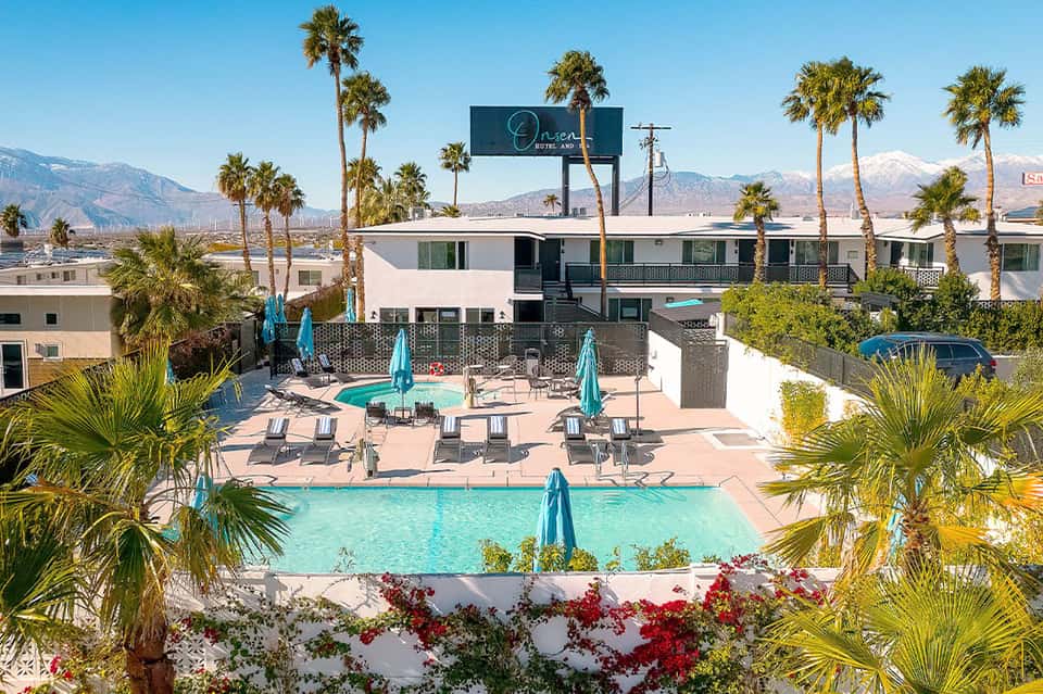 Boutique hotel pools with mountain and palm tree views, turquoise water, lounge chairs, and desert landscape