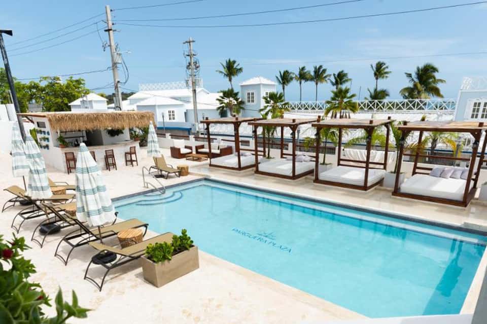 Rooftop pool with lounge chairs, thatched bar, cabanas, palm trees, and ocean view