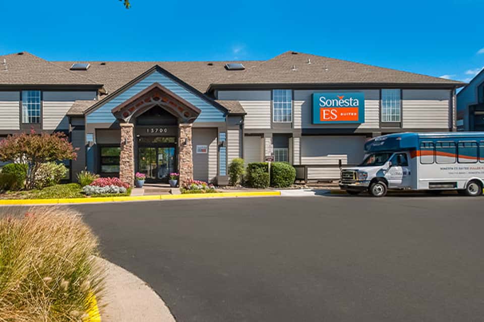 Sonesta ES Suites hotel exterior with stone entrance, professional signage, and shuttle vehicle