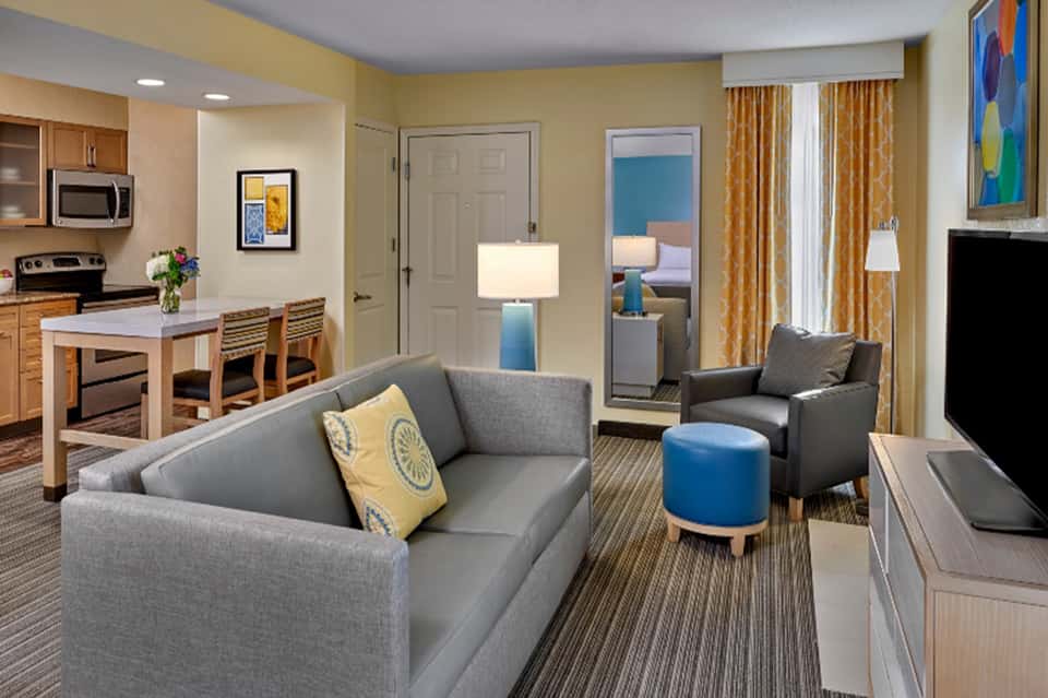 Hotel suite interior with gray sofa, kitchen area, and colorful artwork