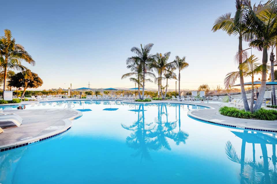 Resort swimming pool with palm trees reflected in calm blue water at sunset