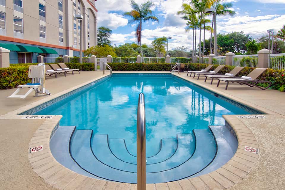 Resort lap pool with lane dividers, lounge chairs, hotel building, and palm trees