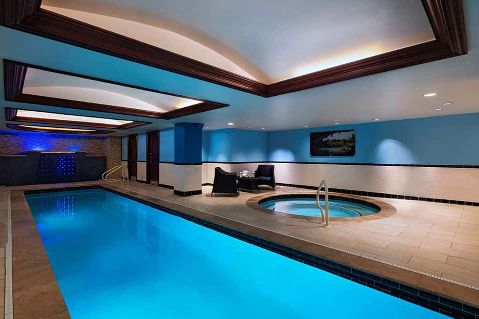 Indoor swimming pool with spa hot tub, blue accent lighting, and modern architectural ceiling