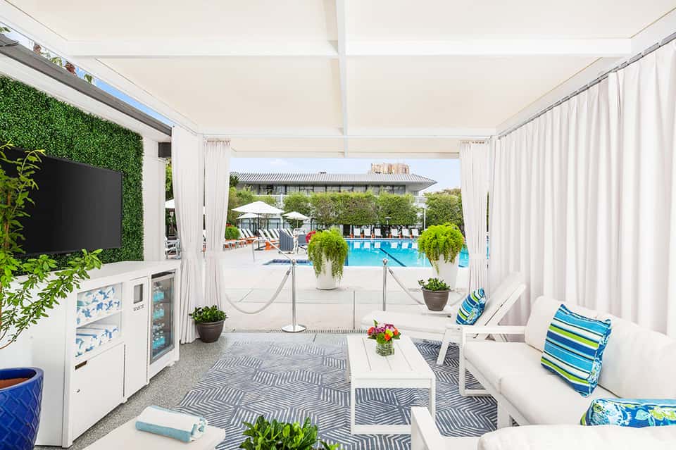 Covered poolside lounge area with white furnishings, TV, views of resort pools and facilities