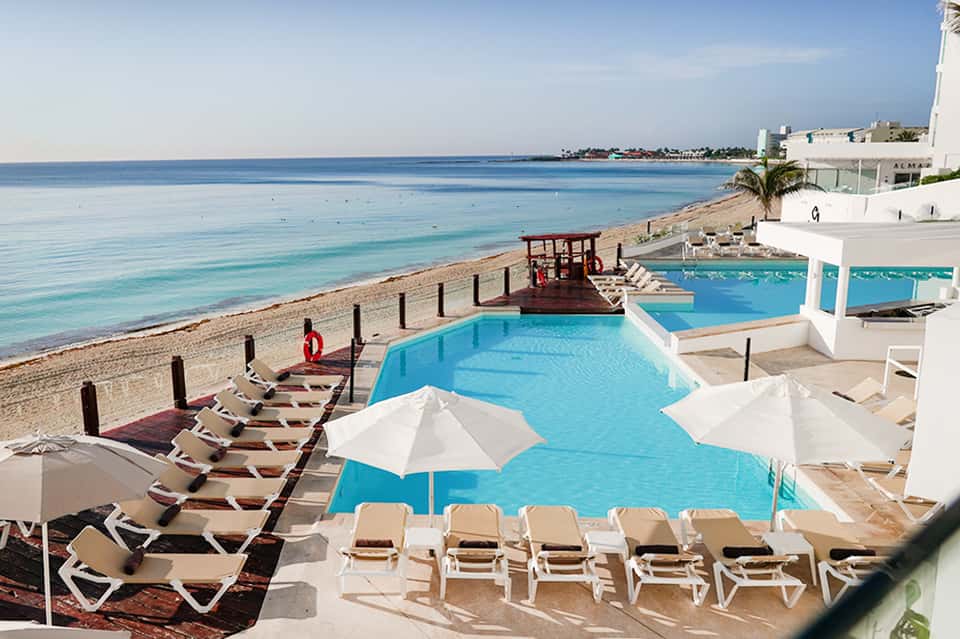 Beachfront resort pools with white umbrellas and turquoise ocean view beyond sandy shore