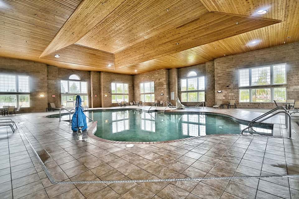 Indoor pool facility with wooden ceiling, brick walls, and multiple lounge areas