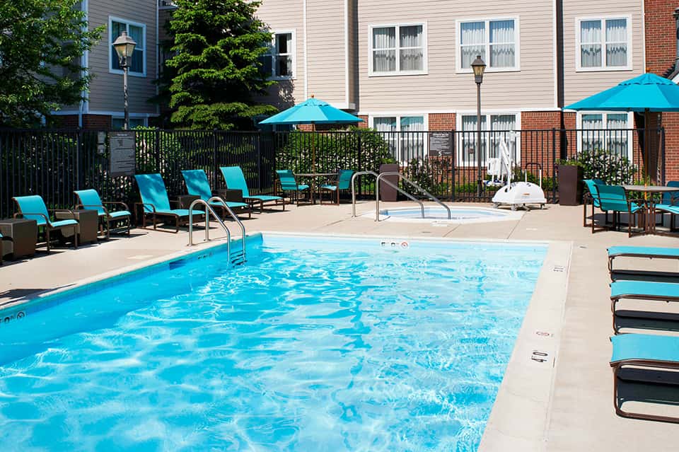 Resort swimming pool with turquoise loungers and umbrellas beside brick building