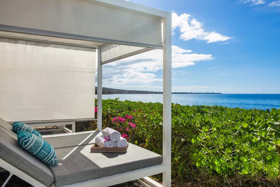 Oceanfront cabana with shade pergola, rolled towels, cushioned seating, and ocean horizon view