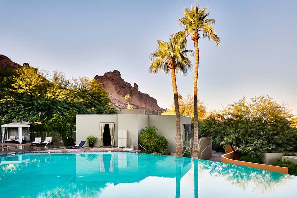 Luxury resort pool with palm trees and desert mountain backdrop at dusk