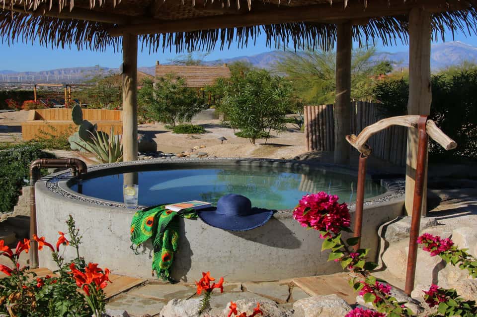 Hot springs pool under palapa roof with mountain views and colorful flowers