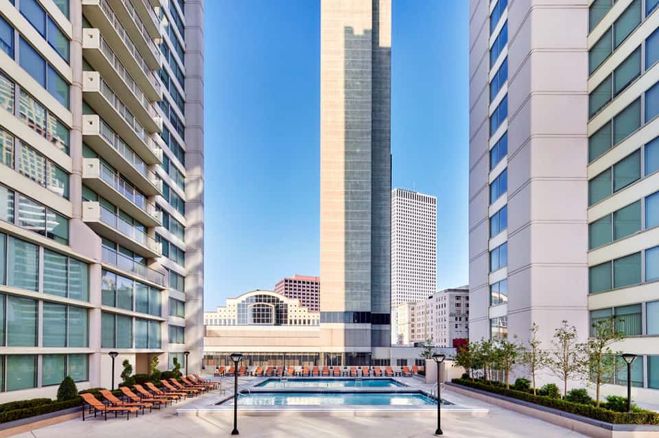 Luxury hotel outdoor pool deck with lounge chairs, twin pools, and surrounding high-rise buildings