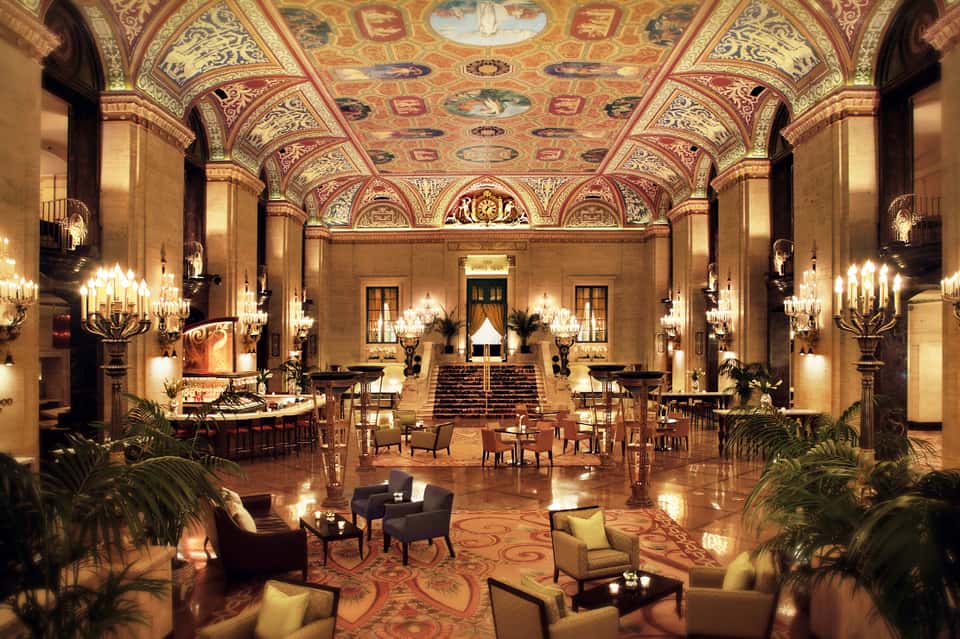 Ornate hotel ballroom with decorated ceiling, crystal chandeliers, elegant furnishings, and grand architecture