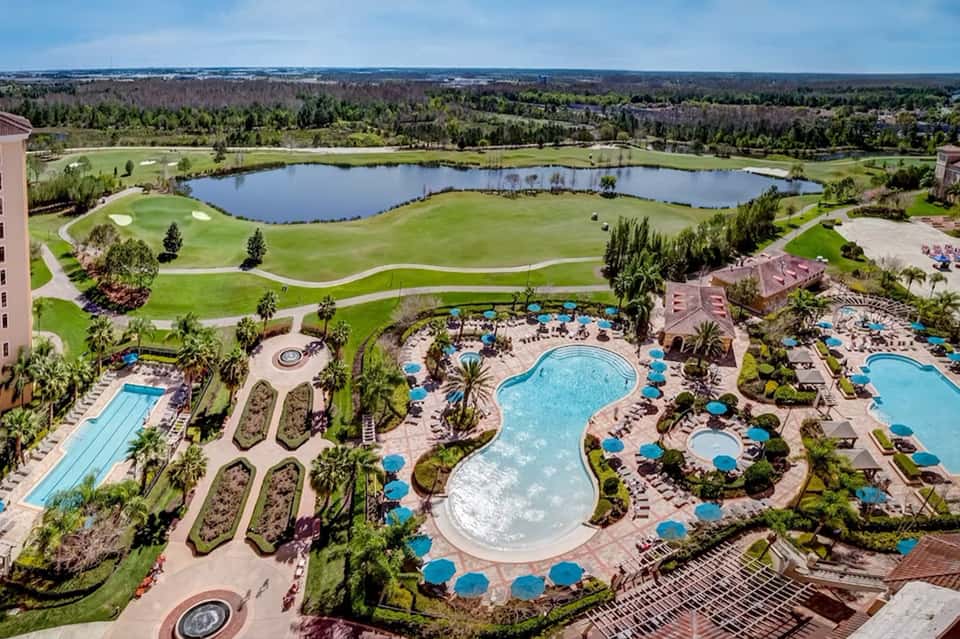 Aerial view of large resort complex with multiple pools, golf course, and lakeside grounds
