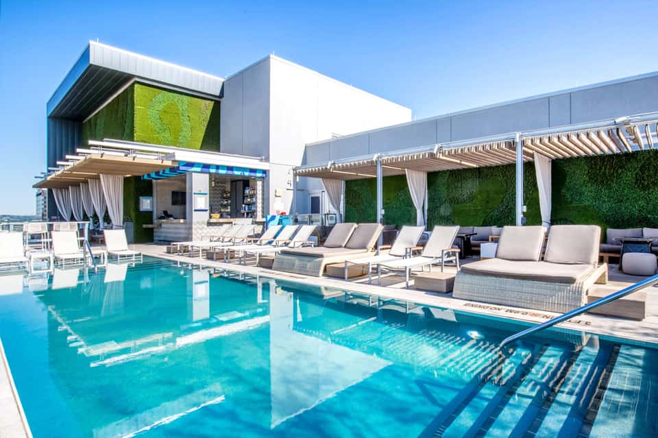 Modern rooftop pool with turquoise water, lounge chairs, pergolas, and contemporary building with green living walls