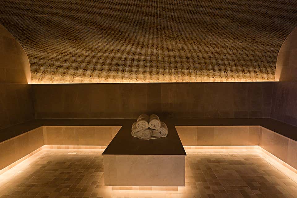 Luxurious spa treatment room with mosaic tile ceiling, heated stone basin, and rolled towels on dark stone platform