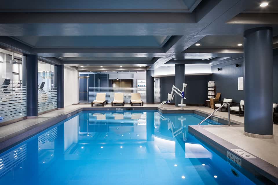 Indoor swimming pool with bright blue water, lounge chairs, and modern architectural columns