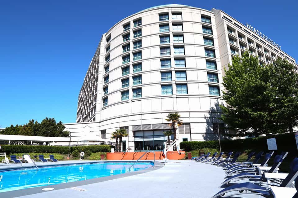 Modern curved hotel building with swimming pool, blue lounge chairs, and landscaping in foreground