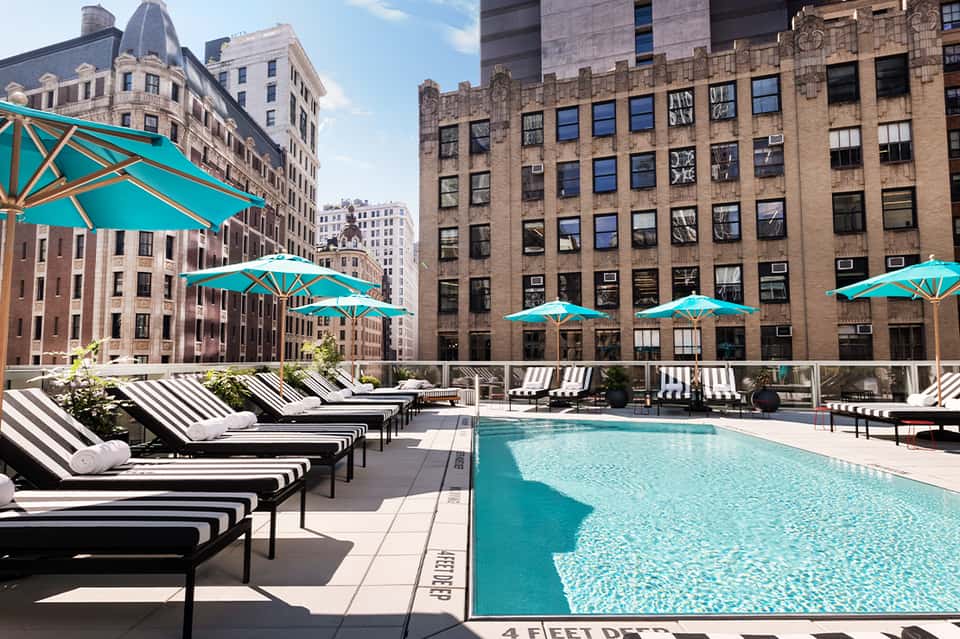 Rooftop pool with turquoise umbrellas and striped lounge chairs overlooking urban skyline