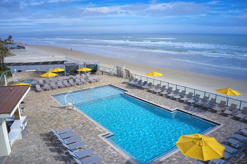 Beachfront resort pool with yellow umbrellas, lounge chairs, and ocean view with waves