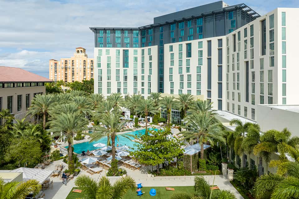 Resort courtyard with expansive pool surrounded by palm trees and modern multi-story hotel buildings