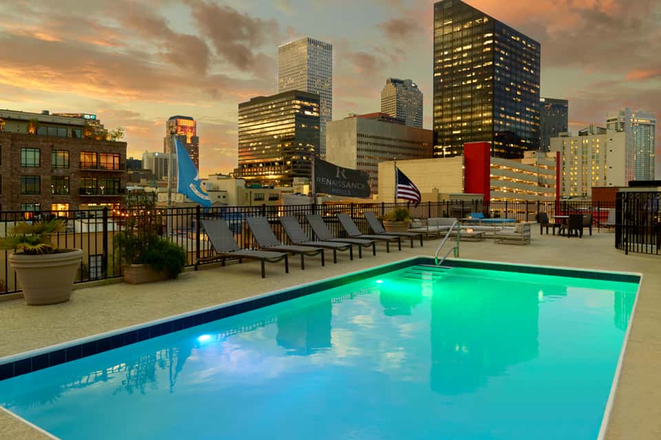 Rooftop pool with turquoise water overlooking city skyline at sunset with lounge chairs