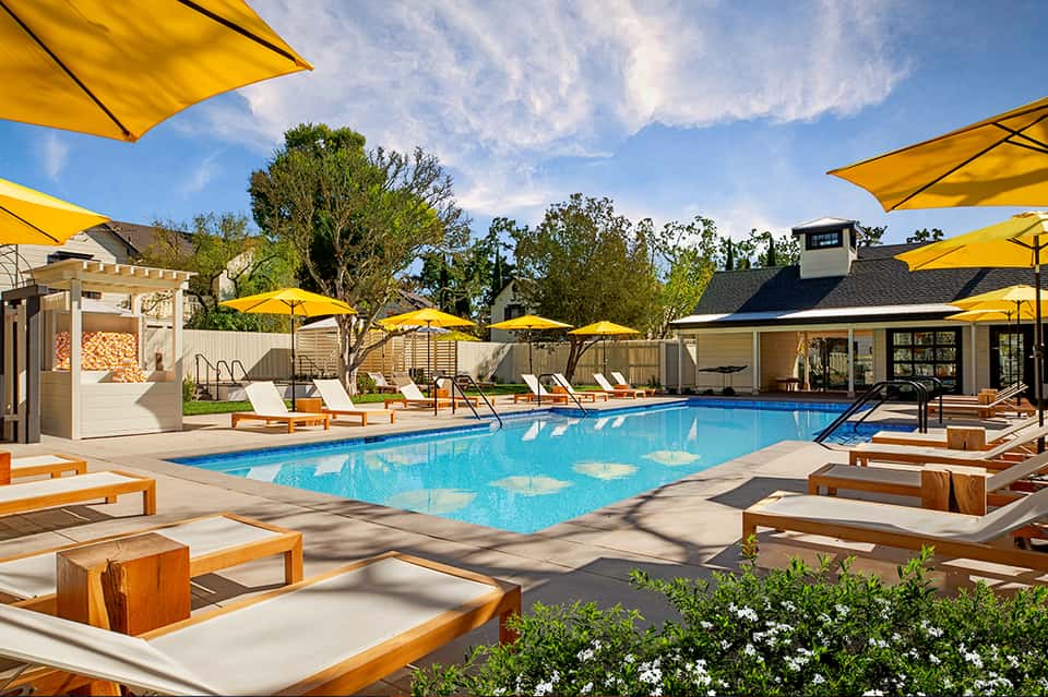 Luxury resort pool with bright yellow umbrellas, lounge chairs, and modern buildings surrounded by manicured landscaping