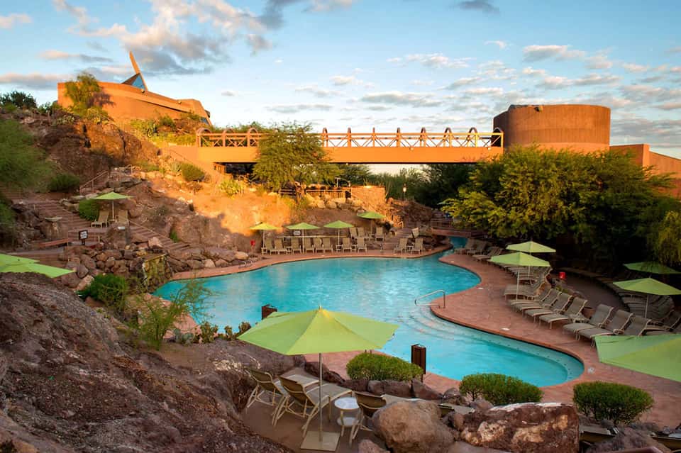 Resort pool with turquoise water, orange umbrellas, and modern architectural structures built into russet cliffs