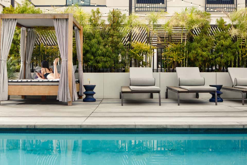 Luxury pool deck with loungers, cabana, bamboo privacy screen, and turquoise water