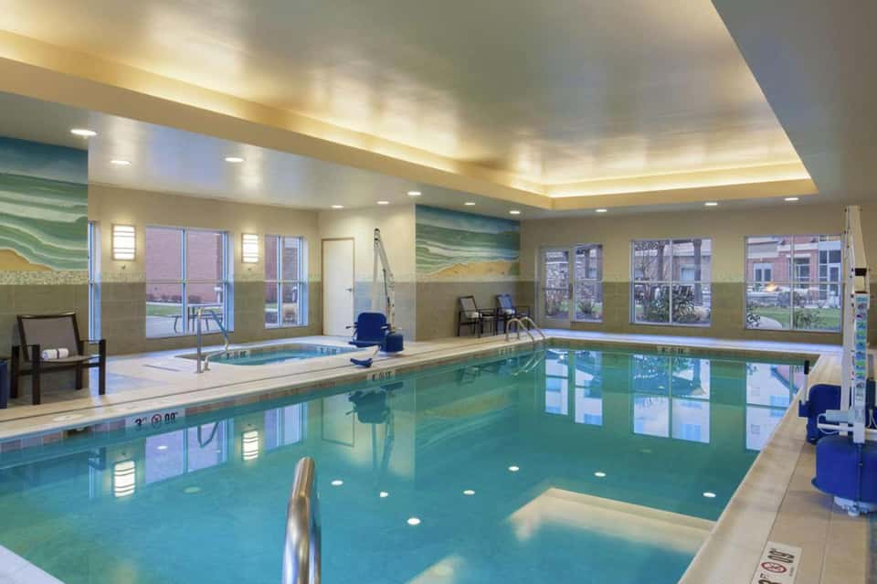 Indoor heated swimming pool with teal water, spa tub, lounge chairs, and large windows overlooking the grounds
