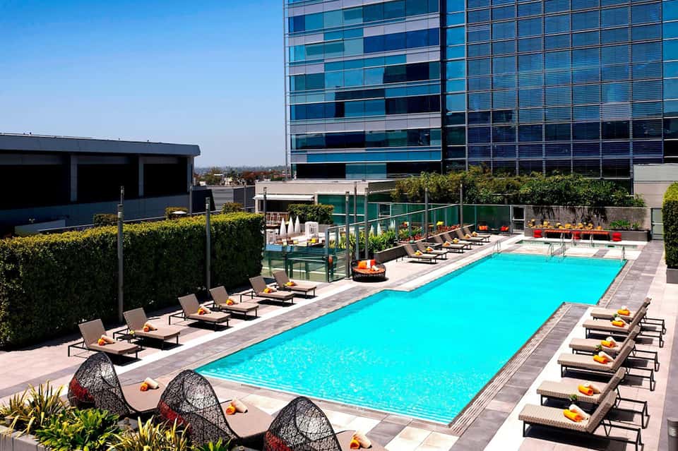 Resort rooftop pool with loungers, fire pit, modern building, and landscaping