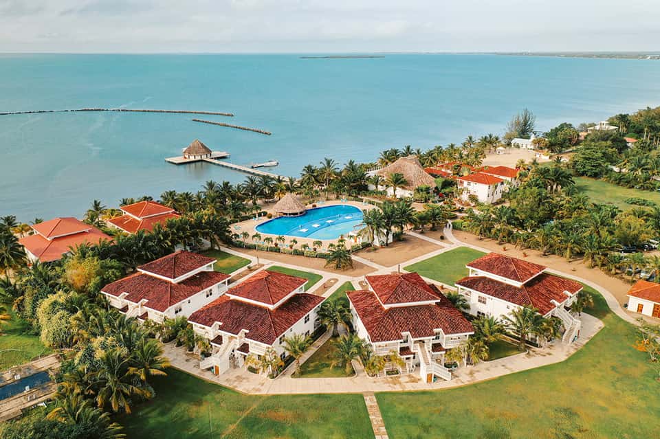 Aerial view of beachfront resort with red-roofed villas, pool, palm trees, and turquoise ocean