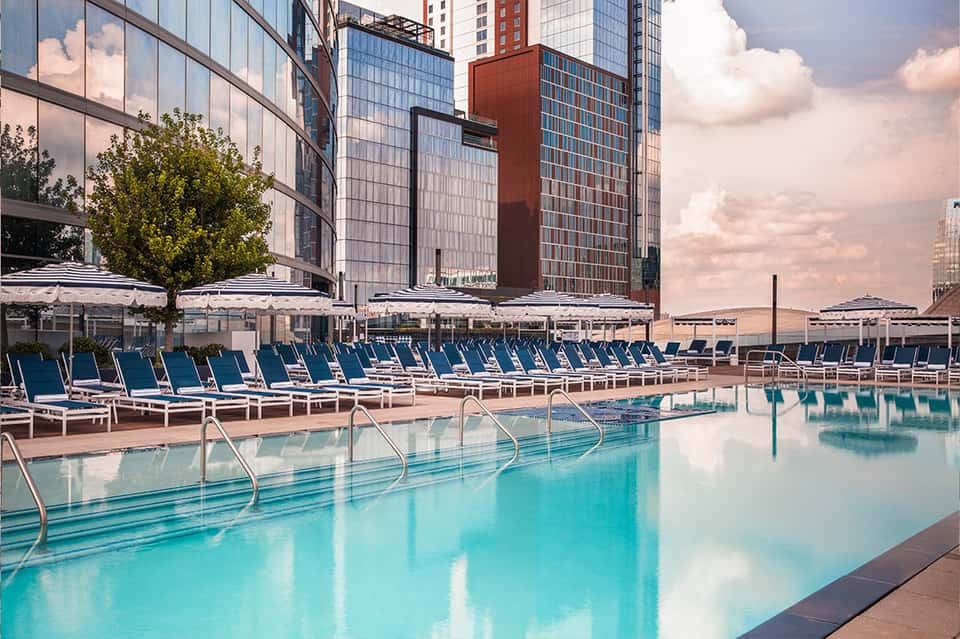 Urban rooftop pool with lounge chairs, umbrellas, and city skyline backdrop