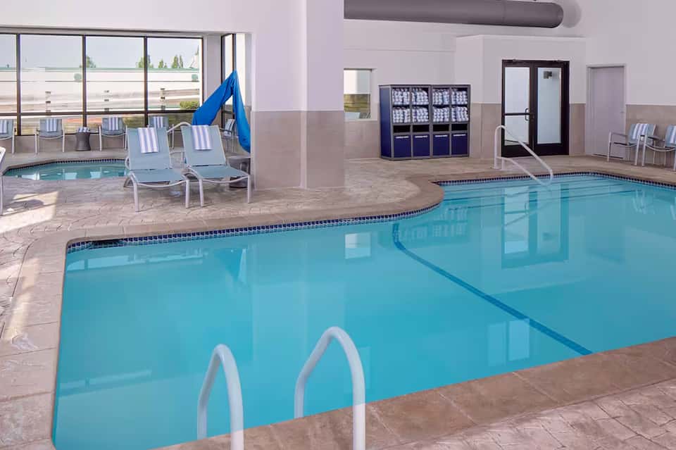 Indoor heated swimming pool with bright blue water, lounge chairs, slide, and large windows overlooking landscape