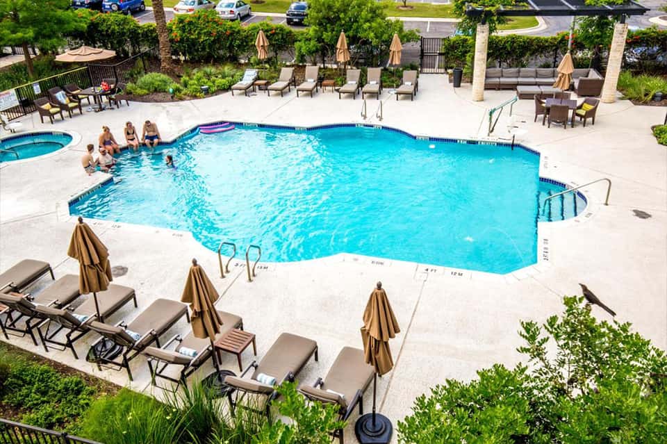 Aerial view of resort pool with guests, loungers, umbrellas, and manicured landscaping