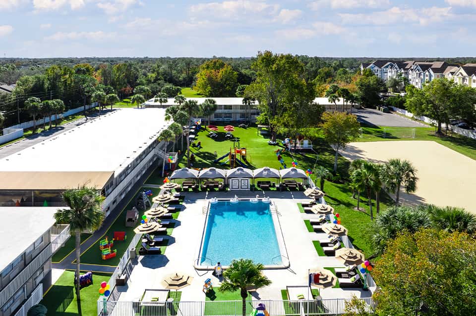 Aerial view of resort pool with loungers, cabanas, and manicured grounds surrounded by residential buildings