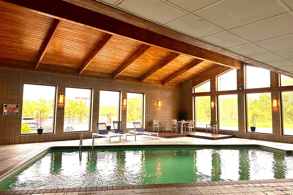 Indoor swimming pool facility with green water, wooden beam ceiling, and large windows overlooking grounds