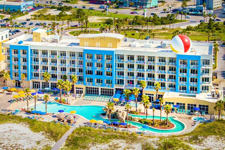 Bright blue resort building with pool and waterslide near beach with palm trees