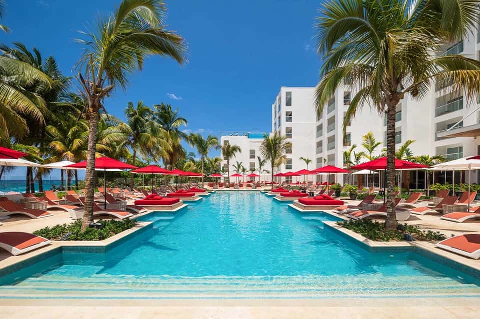Resort pool with turquoise water, red loungers, red umbrellas, and white residential building