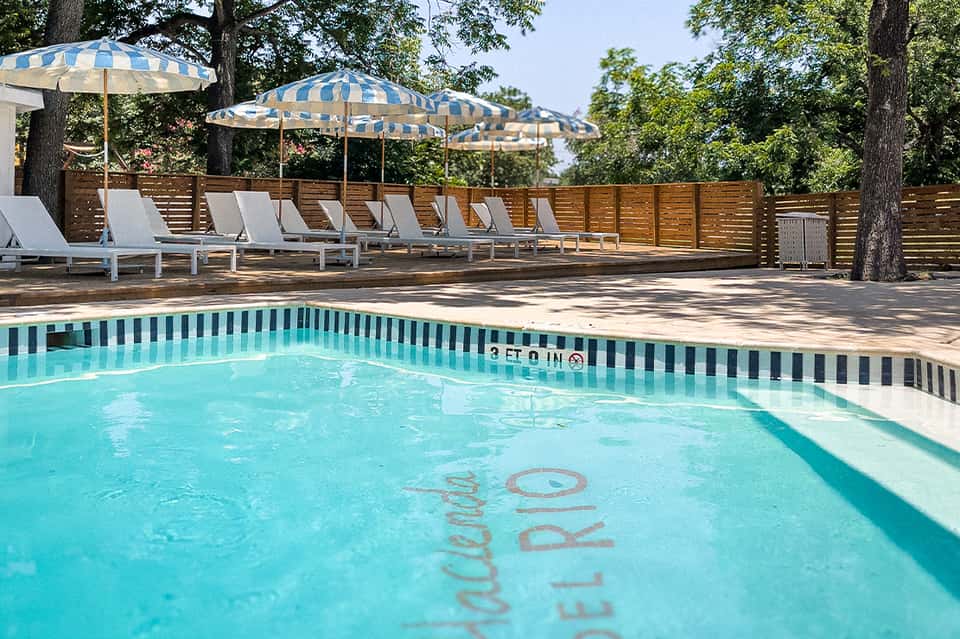 Outdoor pool area with striped umbrellas, lounge chairs, and wooden fence
