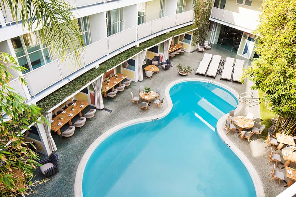 Aerial view of curved swimming pool surrounded by modern hotel buildings with lounge chairs and dining areas